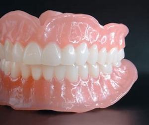 A complete set of dentures showing pink acrylic gum base with white artificial teeth against a dark background.